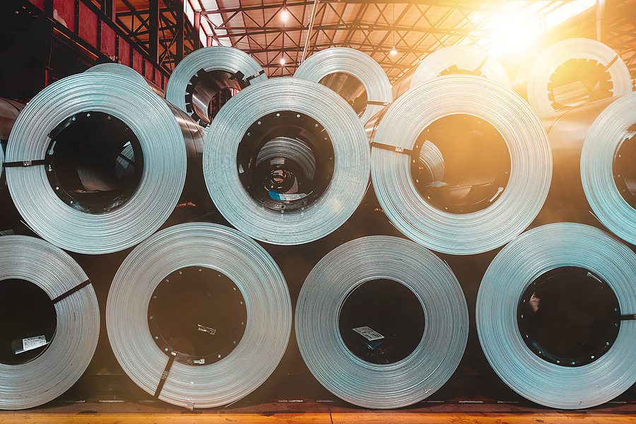 Large rolls of steel inside a warehouse with sunlight coming through ceiling