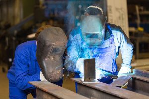 Two welders wearing protective gear work together during a training session. 