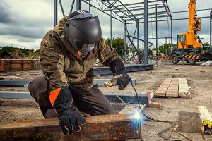 Welder wearing mask and gloves working on a project in a construction site.